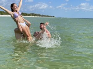Group of friends playing and splashing in the shallow water near a beach on a sunny day.