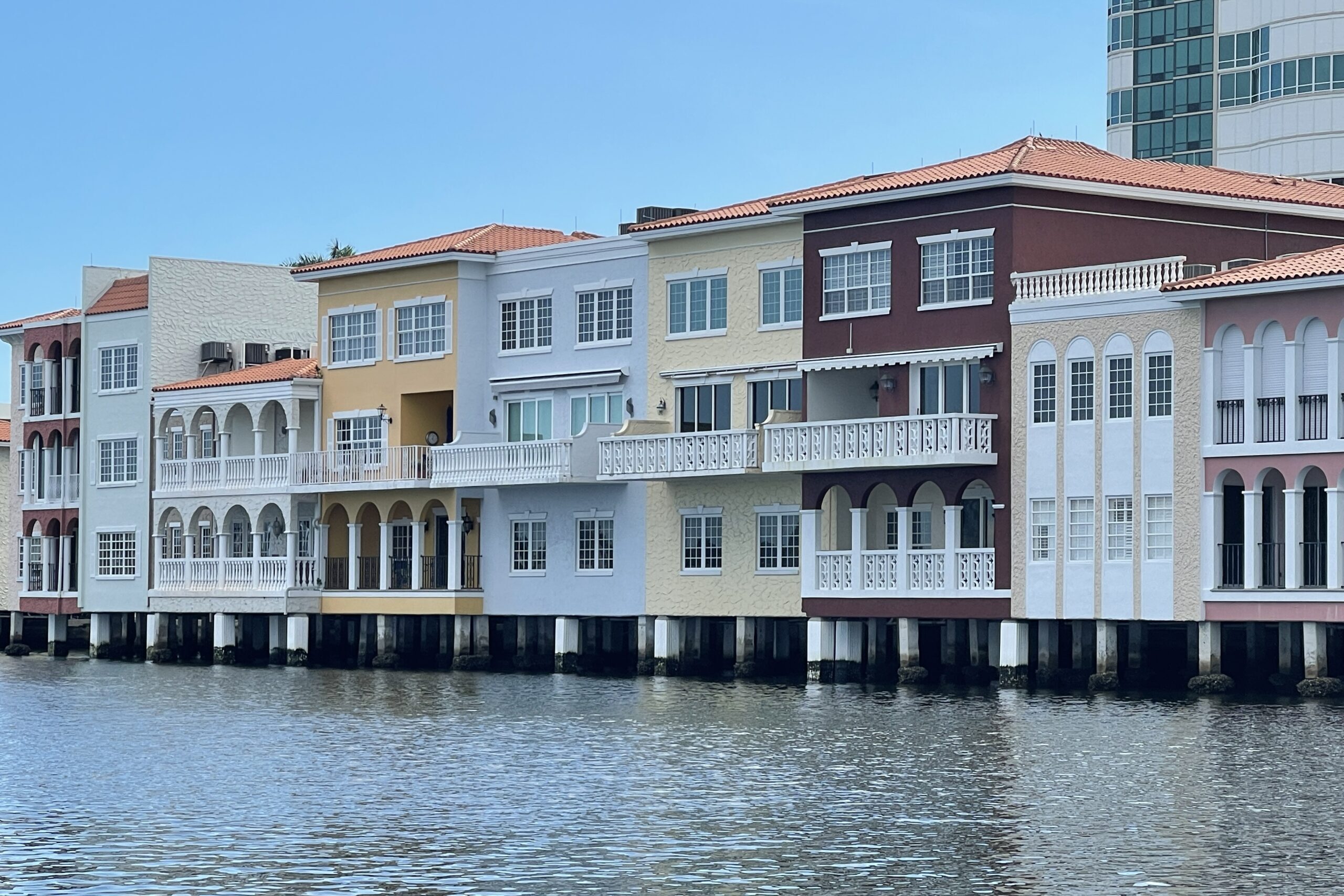 Row of colorful Mediterranean-style waterfront homes with balconies overlooking a calm canal in Naples, Florida.
