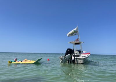 A person lounges on a yellow float in the water behind a center console boat flying a Piano Piano Charters flag