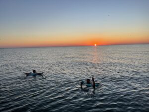 Two people floating in the Gulf of Mexico at sunset, holding drinks and enjoying a Naples boat day off the coast of Keewaydin Island.