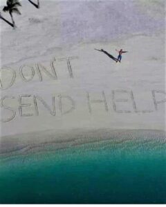 Drone shot of a person on a secluded beach next to large letters in the sand reading “DON’T SEND HELP” with turquoise water below.