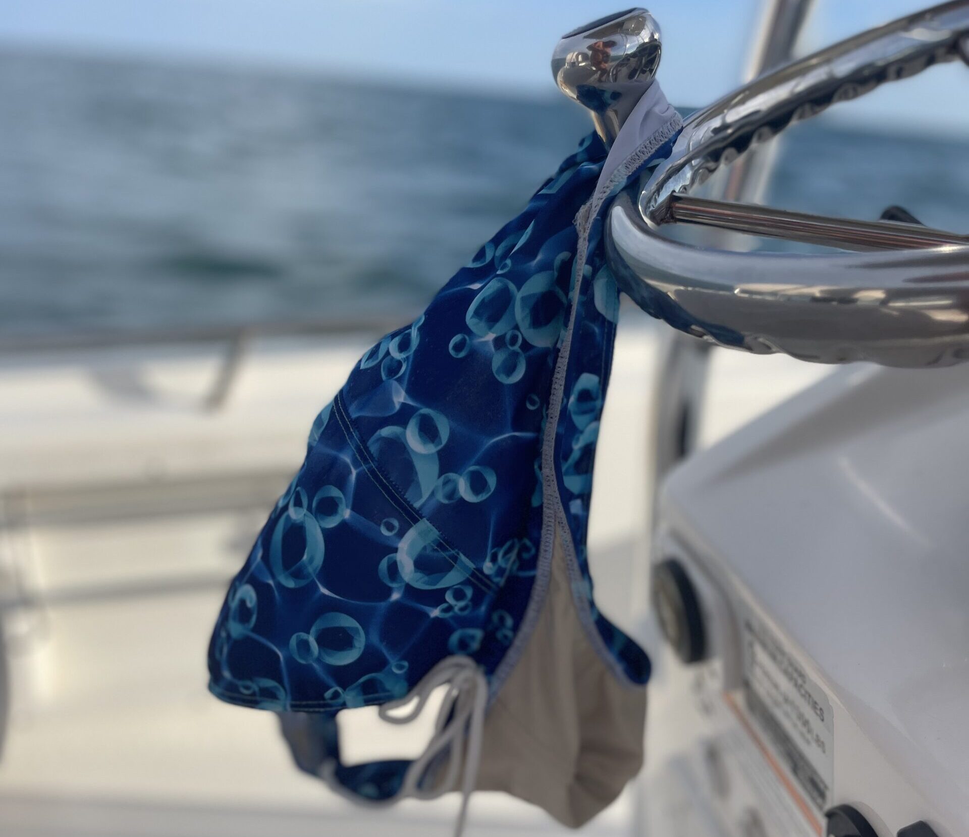 A bikini top hanging from the helm of a boat with the Gulf of Mexico in the background, suggesting a carefree and clothing-optional vibe.