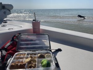 Waterproof snack tackle box on a boat with a tumbler and a dog running along the beach in the background