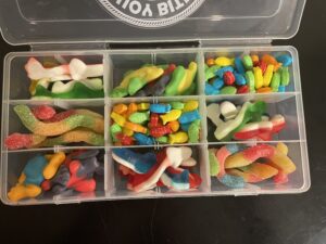 Waterproof tackle box filled with colorful gummy candies including worms, sharks, fish, bones, and other assorted sweets