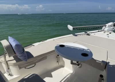 Front seating area of a boat with a small white table, pillow, and trolling motor, facing calm green water
