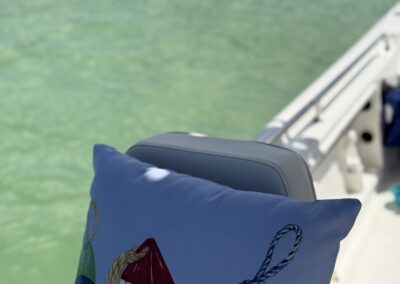 Close-up of a blue decorative pillow with buoy illustrations on a boat, with green water and floating loungers in the background