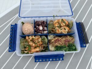 Waterproof tackle box on a boat table filled with grilled shrimp, ahi tuna, crab salad, and octopus