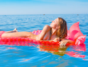 Woman floating nude on the water, eyes closed, embracing coastal freedom and natural beauty.