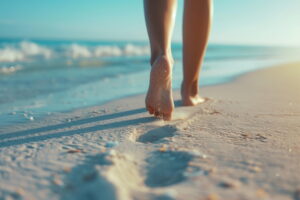 Close-up of barefoot person walking along the sandy beach with ocean waves in the background