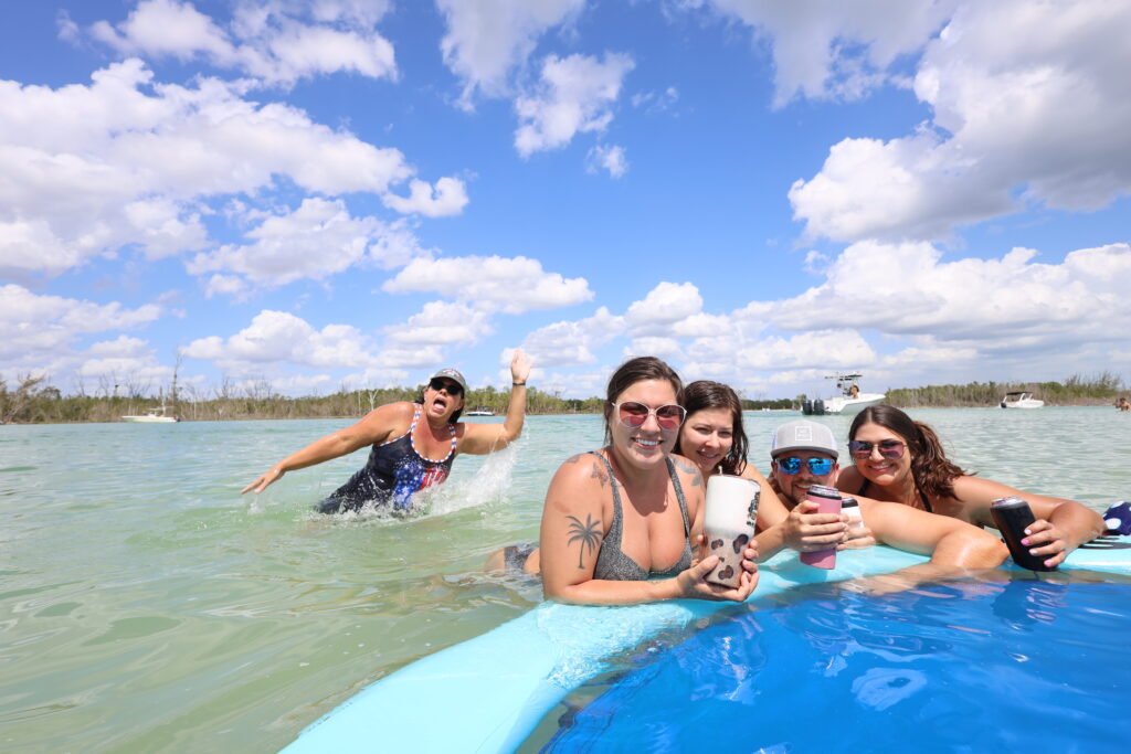 Group of friends lounging on a float in shallow water with drinks in hand, enjoying a sunny beach day near Naples, Florida.