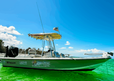 Side view of Piano Piano, a 22-foot center console bay boat, floating near a sandy beach in Naples, Florida, on calm, clear Gulf waters with no one onboard.