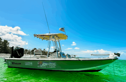 Side view of Piano Piano, a 22-foot center console bay boat, floating near a sandy beach in Naples, Florida, on calm, clear Gulf waters with no one onboard.