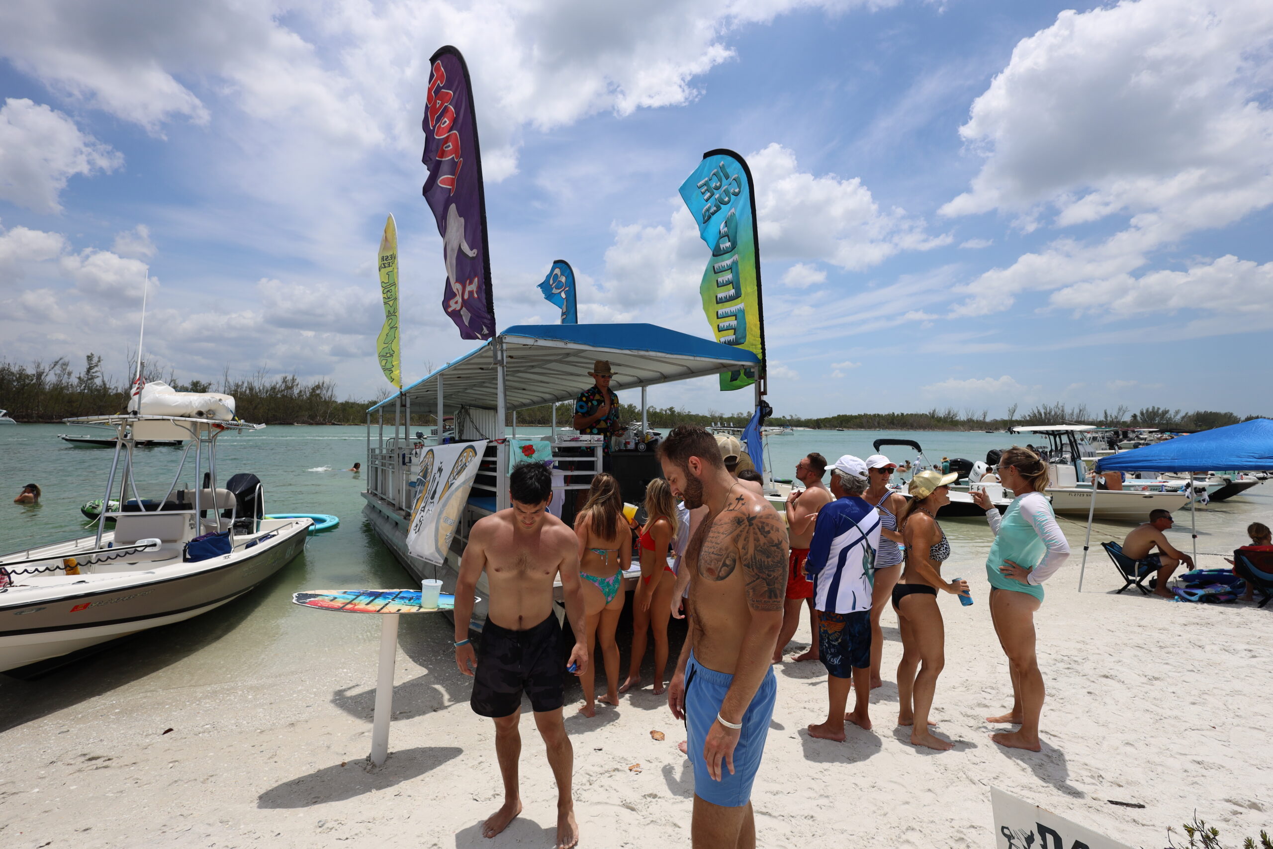 Crowd of people gathered around a floating bar at Keewaydin Island with boats anchored nearby on a sunny day in Naples, Florida.